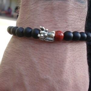 May include: Black beaded bracelet with a silver dragon charm and a red bead. The bracelet is made of lava rock and onyx beads.