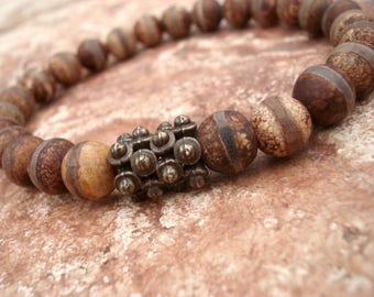 May include: A brown and white agate beaded bracelet with a silver metal bead in the center.