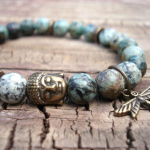 May include: A turquoise and white stone beaded bracelet with a brass Buddha charm and a dragonfly pendant.