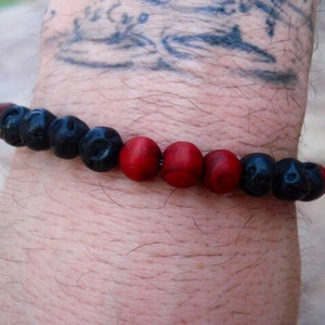 Puede incluir: Un brazalete de cuentas negras y rojas con un diseño sencillo. El brazalete está hecho de pequeñas cuentas redondas.