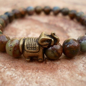 May include: A brown and green gemstone bracelet with a brass elephant charm. The bracelet is made of round beads with a mottled pattern.