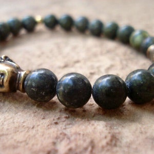May include: A dark green beaded bracelet with a gold Buddha head charm. The beads are round and have a speckled appearance.