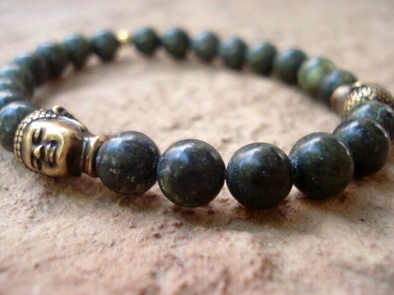 May include: A dark green beaded bracelet with a gold Buddha head charm. The beads are round and have a speckled appearance.
