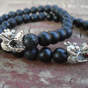 May include: Two black beaded bracelets with silver dragon head charms. One bracelet has a red bead.