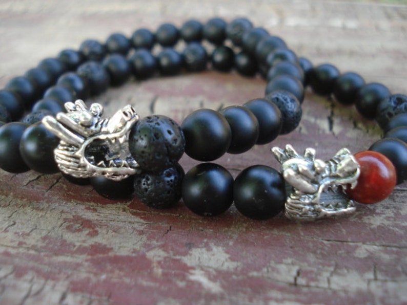 May include: Two black beaded bracelets with silver dragon head charms. One bracelet has a red bead.