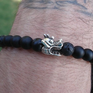 May include: Black beaded bracelet with a silver dragon charm. The beads are made of lava rock and onyx.