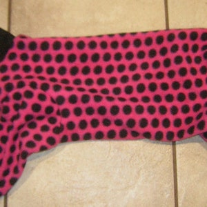 Puede incluir: Pijama para mascotas de lunares rosas y negros. El pijama está hecho de un material de vellón suave. El cuello y los puños son negros. El pijama está diseñado para un perro o gato pequeño.