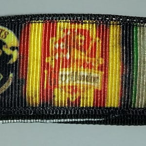 May include: A black ribbon featuring the Hogwarts crest and house emblems. The ribbon displays the Hogwarts crest, along with the Gryffindor, Hufflepuff, and Slytherin house emblems. The ribbon is approximately 1 inch wide.