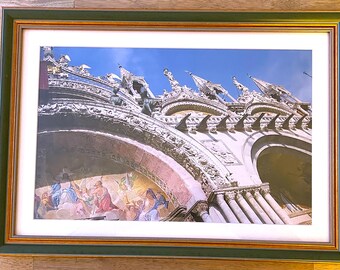Puede incluir: Impresión enmarcada de una arquitectura detallada con tallas ornamentadas, arcos y estatuas sobre un cielo azul. La impresión está en un marco verde y dorado, adecuada para la decoración del hogar.