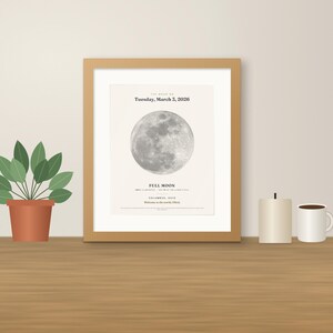 May include: A framed wall art print featuring a detailed greyscale image of a full moon. The text reads: The moon on Tuesday, March 3, 2026, Full Moon, Columbus, Ohio, Welcome to the world, Olivia. The print is housed in a light wood frame.