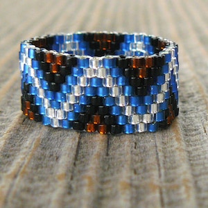 May include: A beaded ring with a geometric pattern in shades of blue, black, white, and brown.