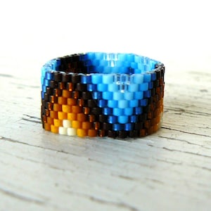 May include: A beaded ring with a blue, brown, and orange geometric pattern.