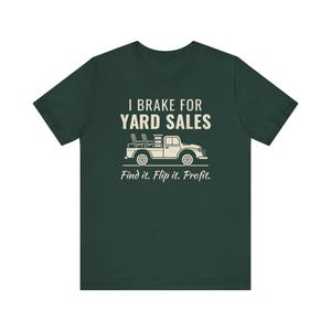 Puede incluir: Una camiseta de manga corta de color verde oscuro con un gráfico en color crema de una camioneta que transporta muebles. El texto dice I BRAKE FOR YARD SALES y Find it. Flip it. Profit. en una combinación de fuentes sans-serif y script.