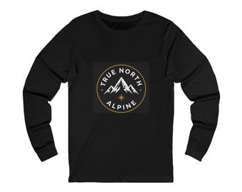 May include: A black long-sleeve shirt featuring a circular graphic on the chest. The graphic contains a white mountain range illustration, a gold star, and the text TRUE NORTH ALPINE in a circular gold border against a dark background.