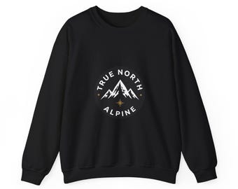 May include: A black long-sleeve sweatshirt featuring a circular graphic on the chest. The design includes white mountain peaks, a gold star icon, and the text "TRUE NORTH ALPINE" printed in white lettering around the circular border.