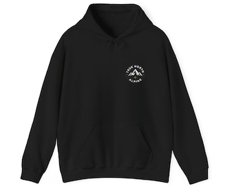 May include: A black hooded sweatshirt featuring a front kangaroo pocket and a circular graphic on the left chest. The graphic displays a white mountain range illustration with the text True North Alpine and a small star icon below the peaks.