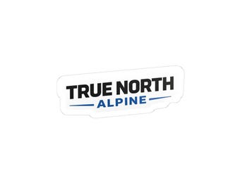 May include: A die-cut sticker featuring the text TRUE NORTH in bold black capital letters, with the word ALPINE in blue capital letters underneath, flanked by two horizontal blue lines on a white background.