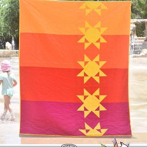 May include: A rectangular quilt titled Heat Wave featuring a vertical gradient of orange, red, and magenta horizontal bands. A column of five yellow star-shaped quilt blocks runs down the center. The quilt has a yellow border and wavy stitching.