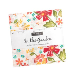 May include: A stack of square fabric pieces featuring a floral pattern with red, orange, yellow, and teal flowers on a white background. A white paper band wraps around the centre, displaying the text "In the Garden" and a 12.7 cm ruler scale.
