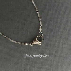 May include: A silver-toned metal chain necklace featuring a lobster claw clasp closure. The delicate chain links are connected to the clasp mechanism. The text Jmes Jewelry Box is printed in white lettering at the bottom of the image.