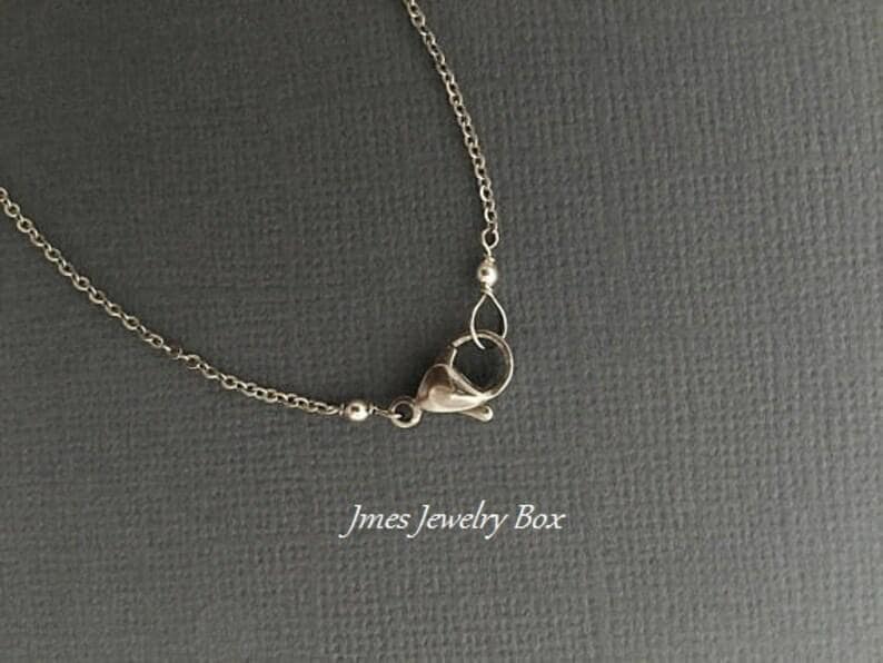 May include: A silver-toned metal chain necklace featuring a lobster claw clasp closure. The delicate chain links are connected to the clasp mechanism. The text Jmes Jewelry Box is printed in white lettering at the bottom of the image.