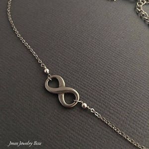 May include: A silver infinity symbol pendant necklace with a delicate chain. The pendant is attached to the chain with two small silver beads.