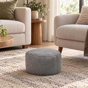 May include: A round, low-profile ottoman upholstered in a textured, heathered gray fabric. The cylindrical footstool features a simple, seamless design with a flat top and vertical sides, resting directly on the floor surface.