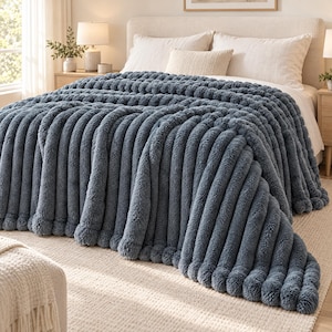 May include: A dark blue plush throw blanket with a thick, vertical ribbed texture. The blanket features a soft, fuzzy material and is draped over a bed, showcasing its deep color and prominent, raised channel-stitched design throughout.