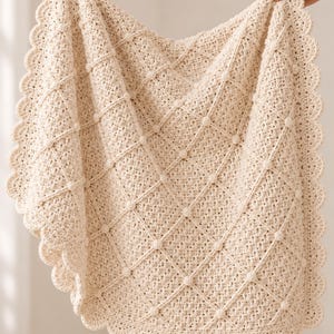 May include: A cream-colored crochet blanket featuring a diamond lattice pattern with small raised bobbles at each intersection. The blanket is finished with a decorative scalloped edge border that runs along the entire perimeter of the piece.