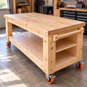 May include: A rectangular wooden workbench featuring a thick light-coloured wood top, a lower storage shelf, and a side handle. The structure is supported by four heavy-duty swivel castors with bright orange wheels, allowing for mobility.