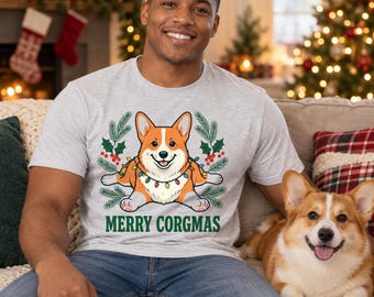 May include: A light gray short-sleeve t-shirt featuring a graphic of a Corgi dog wrapped in colorful Christmas lights, surrounded by pine branches and holly berries, with the green text MERRY CORGMAS printed below the illustration.