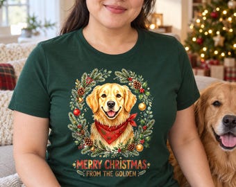 May include: A dark green t-shirt featuring a graphic of a golden retriever wearing a red bandana, surrounded by a Christmas wreath of pine branches, pinecones, and ornaments, with the text Merry Christmas From The Golden.