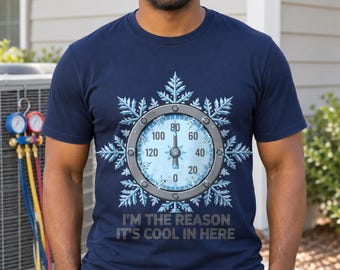 Pode incluir: Uma t-shirt azul-marinho de manga curta com um gráfico de um manómetro circular centrado num grande floco de neve branco detalhado. O medidor tem um ponteiro a apontar para cima e o texto "I'M THE REASON IT'S COOL IN HERE" impresso por baixo.