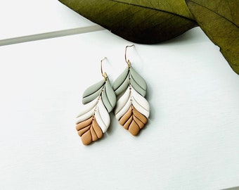 May include: A pair of dangle earrings with a layered leaf design. The leaves are made of polymer clay and are painted in shades of brown, white, and green. The earrings are attached to gold-colored hooks.