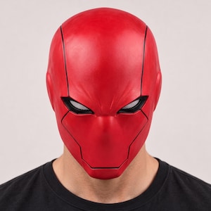 Op de afbeelding: Een rood masker voor het hele hoofd met een gladde, matte afwerking en zwarte verzonken paneellijnen. Het masker heeft smalle, hoekige oogopeningen met witte gaasinzetstukken en bedekt het gehele gezicht en hoofd.