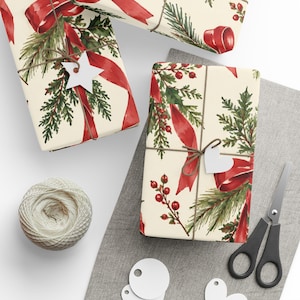 May include: Two rectangular gift boxes wrapped in cream-colored paper featuring a festive pattern of red ribbons, green pine branches, and red berries. Each box is tied with brown twine and includes a small white star or heart-shaped gift tag.