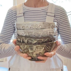 May include: A stack of four ceramic bowls with a white glaze and brown and black patterns. The bowls are stacked in a person's hands.