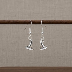 May include: A pair of silver-toned dangle earrings featuring a small, three-dimensional witch hat charm. Each earring is suspended from a standard silver-toned metal fishhook ear wire, showcasing a polished metallic finish and a pointed hat design.