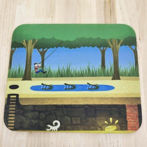 May include: A rectangular mousepad featuring a colorful illustration of a person swinging on a vine over a blue pond with three crocodiles. Below the ground level, a dark stone tunnel contains a white scorpion and a glowing gold bar.