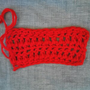 May include: A red crocheted rectangle with a loose end of yarn. The crochet is a simple stitch pattern.