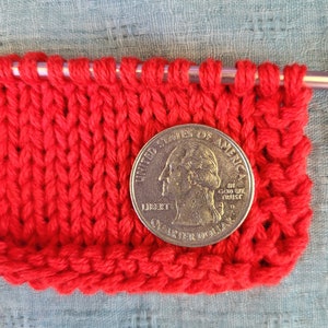 May include: Red knitted fabric with a US quarter dollar coin on top. The coin features the profile of George Washington and the words "United States of America, In God We Trust, Liberty, Quarter Dollar".