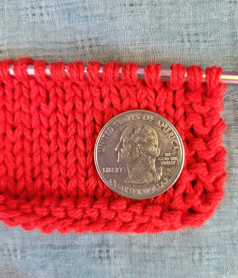 May include: Red knitted fabric with a US quarter dollar coin on top. The coin features the profile of George Washington and the words "United States of America, In God We Trust, Liberty, Quarter Dollar".