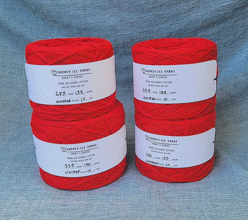 May include: Three spools of red yarn labeled "Audrey Lee Yarns" with the text "Unknit & Remake 100% Reclaimed Cotton Machine Wash and Dry" and the yardage and weight of each spool.