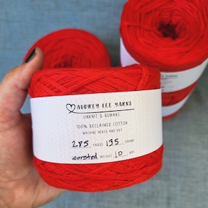 May include: A red ball of yarn with a white label that reads "Audrey Lee Yarns, Unknit & Remake, 100% Reclaimed Cotton, Machine Wash and Dry, 285 Yards, 135 Grams, Worsted Weight 10 WPI."