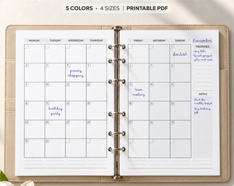 Può includere: Un'agenda mensile su due pagine con un meccanismo di rilegatura a sei anelli in metallo. La carta bianca presenta una griglia per novembre, incluse sezioni per priorità e note scritte a mano. Il testo recita MONTHLY PLANNER ON 2 PAGES.