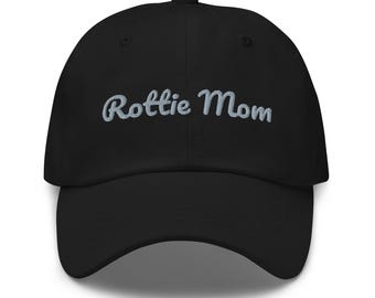 May include: A black baseball cap featuring the text "Rottie Mom" embroidered in light gray script lettering across the front panel. The cap has a structured crown, a curved brim, and a classic six-panel design with ventilation eyelets.