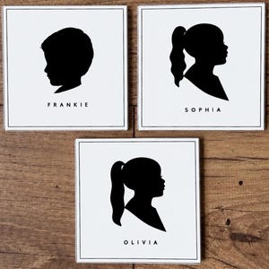 May include: Three square white tiles featuring black silhouette profiles of heads. The top left tile shows a profile labeled FRANKIE, the top right tile shows a profile labeled SOPHIA, and the bottom tile shows a profile labeled OLIVIA.