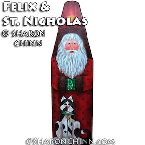 May include: A hand-painted wooden sign featuring Santa Claus with a white beard and a black and white cat. The sign is painted in red, white, green, and black with a gold star on Santa's hat. The text "Felix & St. Nicholas © Sharon Chinn" is written on the sign.