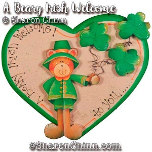 Puede incluir: Un cartel verde en forma de corazón con un oso de dibujos animados que lleva un sombrero verde y sostiene tréboles. El cartel dice "A Beary Irish Welcome" y "Welcome!" con el texto "Beary Irish" escrito verticalmente. El cartel también dice "to you..." en la parte inferior.