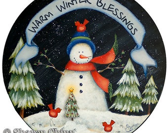 May include: A round, wooden, painted sign with a snowman, two pine trees, a Christmas tree, and three red birds. The sign has a white banner with the text "Warm Winter Blessings" in blue lettering.